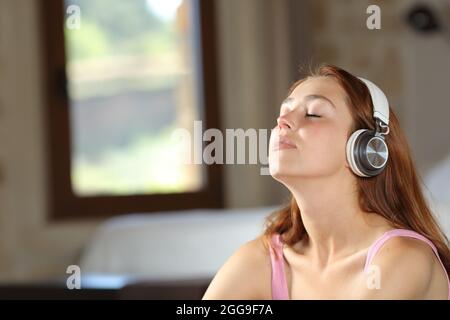 Relaxed woman listening to music wearing headphones and breathing fresh air in a bedroom at home Stock Photo