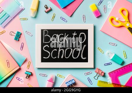 Blackboard with letters Back to school made with chalk. School supplies, pencils, scissors and colored books on blue and pink background. Top view or flat lay. Back to school concept Stock Photo