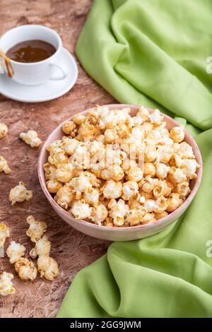 Popcorn with caramel in ceramic bowl on brown concrete background and green textile. Side view, close up. Stock Photo