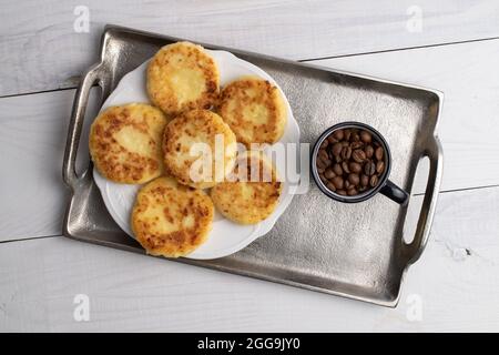 Several fragrant pancakes with a ceramic plate and a cup of coffee on a metal tray, close-up, on a white wooden table, top view. Stock Photo