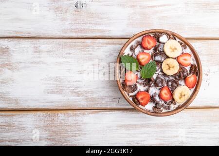 Chocolate cornflakes with milk and strawberry in wooden bowl on white wooden background. Top view, flat lay, copy space. Stock Photo