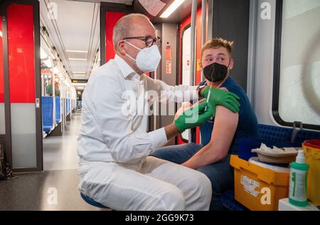 30 August 2021, Berlin: Christian Gravert, chief medical officer of the Deutsche Bahn, vaccinates a man in a special train of the S-Bahn, in which vaccinations with the vaccine of the manufacturer Johnson & Johnson are offered. Photo: Christophe Gateau/dpa Stock Photo