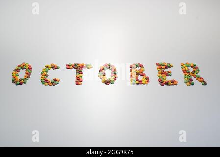October inscription on a white background. Confectionery sprinkles in the form of multi-colored maple leaves Stock Photo