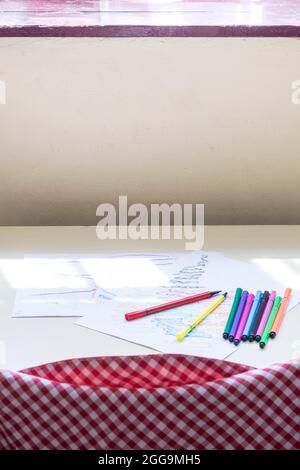 Photograph of colour ed markers and a drawing of a child on a table in a classroom of a nursery school.The photo is taken in vertical format. Stock Photo