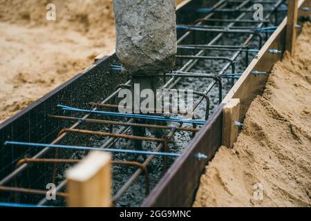 Pouring cement or concrete with automatic pump, construction site with reinforced grillage foundation, start of new house building construction. Stock Photo