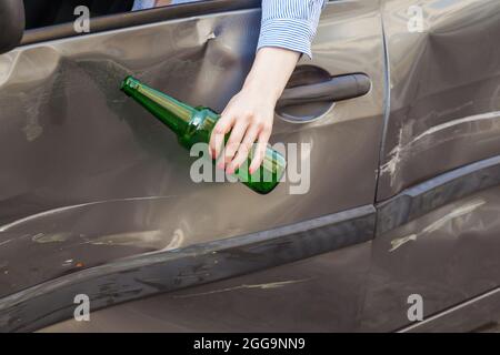 Faceless portrait of female hand hanging from the car window with bottle of alcohol beverage, breakdown due to drunk driver, traffic offenses drunk dr Stock Photo