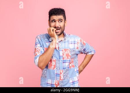 Anxiety disorder. Portrait of stressed out, worried man in blue casual shirt biting nails, nervous about troubles, panicking and looking scared. Indoo Stock Photo