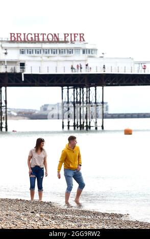 Brighton UK 30th August 2021 - A couple go for a paddle on Brighton beach on an overcast August bank holiday Monday morning .  : Credit Simon Dack / Alamy Live News Stock Photo