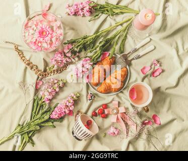 Aesthetic outdoor picnic. Breakfast with croissants, beautiful cups, flowers, burning candles and jewelry scattered on blanket. French style. Top view Stock Photo