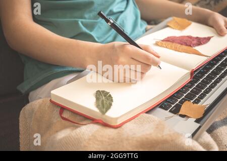 Girl with notebook at home in autumn holidays. Blank diary with autumn leaves close-up Stock Photo