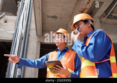 Contractors with tablet computer using walkie-talkie to control work of builders at construction site Stock Photo