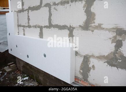 Installing rigid foam board insulation using screws with large washers on the house wall made from large concrete blocks. Stock Photo