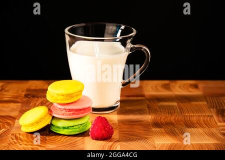 Several colored macarons and a transparent cup with almond milk on a wooden table. Pink, green and yellow macaroons next to a transparent cup of plant Stock Photo