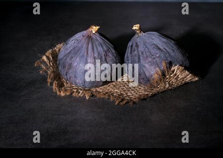 Two ripe purple figs lie on coarse cloth and on a concrete top. Stock Photo