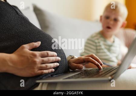 Surprised boy looking at belly of pregnant mother while she working with laptop at home Stock Photo
