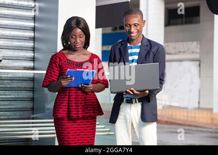 portrait of two african adult businessmen standing outside, man looking at computer and woman looking at his document Stock Photo