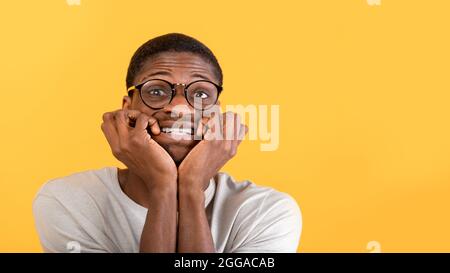 Stress control concept. Afraid black man biting nails with worry, looking at camera over yellow background, panorama Stock Photo