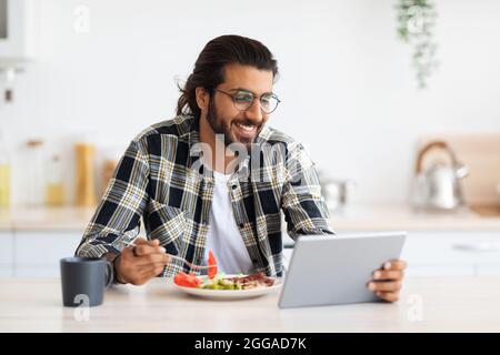 Handsome arab guy having breakfast, using digital tablet, copy space Stock Photo
