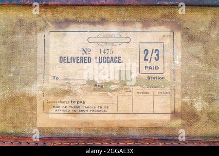 Vintage torn paper luggage label with text delivered luggage on an old leather suitcase Stock Photo