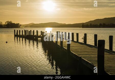 A wooden jetty at the eastern end of Coniston Water in the Lake District National Park on a sunny winter evening Stock Photo