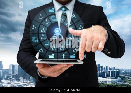 Man In Uniform Standing Holding Tablet And Virtually Tapping Screen. Business Man Carrying Pad Typing And Displaying New Futuristic Technologies. Stock Photo