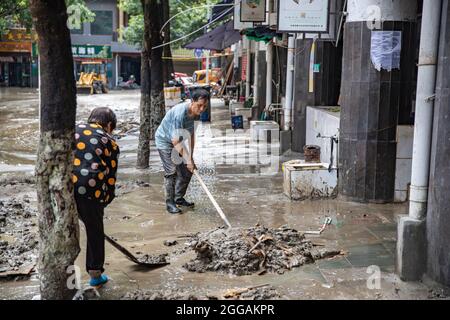 (210830) -- CHONGQING, Aug. 30, 2021 (Xinhua) -- People remove mud on the ground in Wuxi County of Chongqing, southwest China, Aug. 30, 2021. Heavy rain has led to the flooding of four rivers in southwest China's Chongqing Municipality, and more than 2,000 people have been evacuated, according to Chongqing's flood control and drought relief headquarters. In Wuxi County, more than 260 shops were flooded due to constant rain. Local public security and emergency departments have jointly established rescue teams to help shop owners transfer materials and evacuate people who are trapped to safe Stock Photo