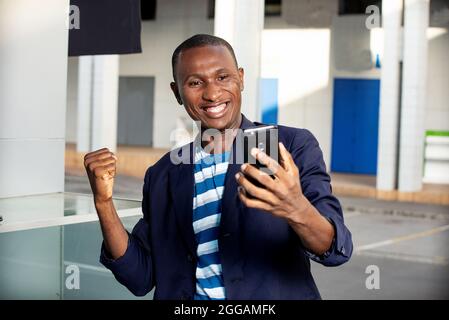 handsome happy adult business man looking at his phone while making a victory gesture with the outside hand Stock Photo