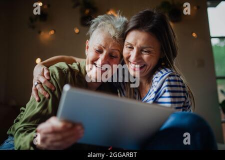 Portrait of happy senior mother with adult daughter indoors at home, using tablet. Stock Photo