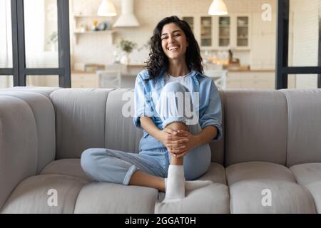 Positive emotions. Portrait of pretty Caucasian woman smiling, laughing and looking at camera, sitting on sofa at home Stock Photo