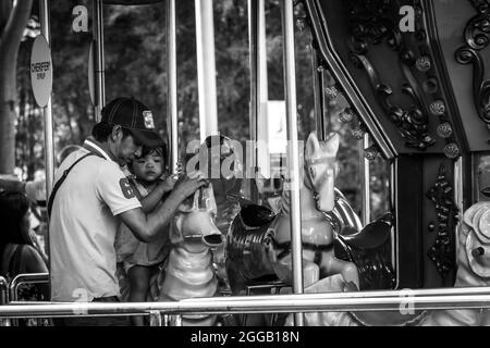 SUBIC, PHILIPPINES - Aug 09, 2017: A grayscale of a father caring for his daughter at a carousel of Subic Bay in Olongapo City, Zambales, Philippines Stock Photo