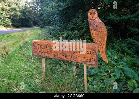 Wooden carved Owl sitting on a carved sign post advertising chainsaw carvings Stock Photo
