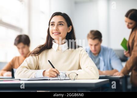 Smiling student sitting at desk in classroom thinking Stock Photo