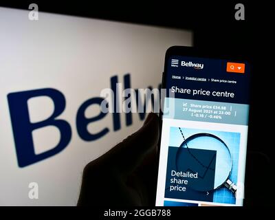 Person holding cellphone with webpage of British property development company Bellway plc on screen with logo. Focus on center of phone display. Stock Photo