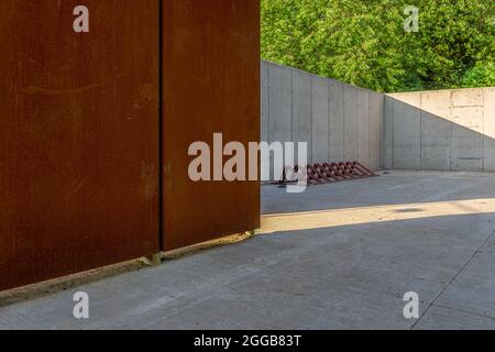 Wall made of architectural concrete and corten sheet surrounded by greenery in the park, a bicycle rack standing on a concrete floor Stock Photo