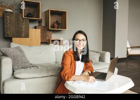 The student studies at home, programs or works as a freelancer. A woman writes with a pen on paper. Stock Photo