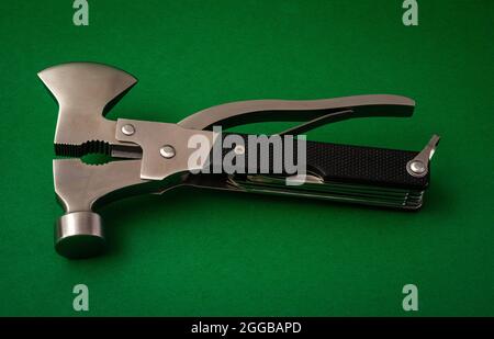camping or survival multi tool , with axe hammer and pliers on green background . Stock Photo