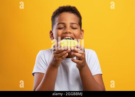 Black boy eating colorful donut, isolated on yellow background Stock Photo