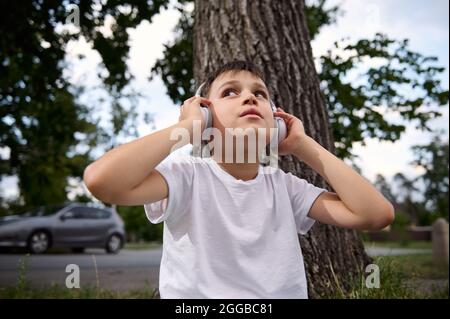 Portrait of handsome boy, wearing wireless headphones and enjoying listening to the music, resting during recreation between classes in the public cit Stock Photo