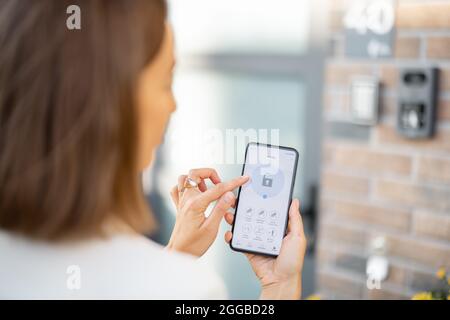 Female closes the door or turns on the house alarm with phone Stock Photo