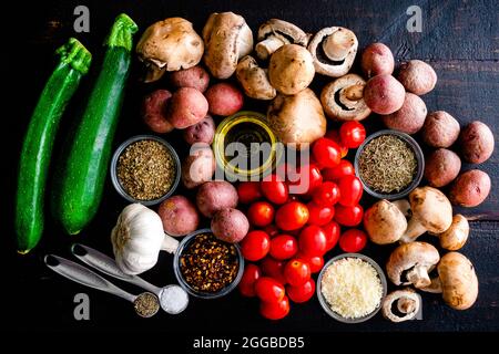 Italian Oven Roasted Vegetables Ingredients on a Wood Table: Grape tomatoes, zucchini, mushrooms, red potatoes, herbs, spices, and olive oil Stock Photo