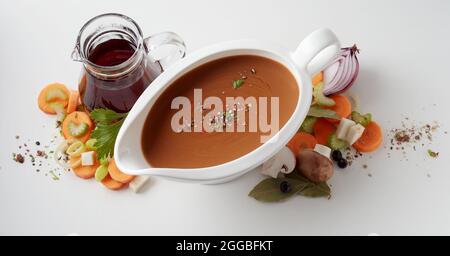 From above of brown vegetable sauce in white oval bowl placed on table with glass cruet with vinegar and scattered cut carrots and onions Stock Photo