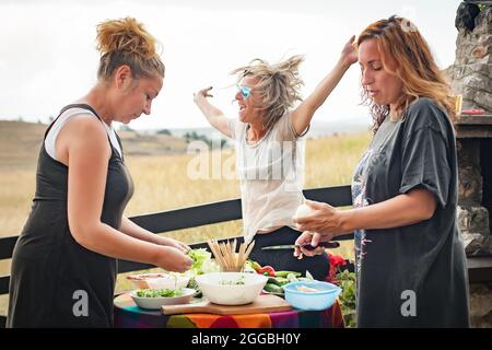 Cheerful and playful friends laughing, dancing and enjoying the mountain ambience and make a barbecue in front of their house Stock Photo