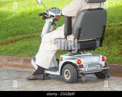 Elderly man dressed in beige clothing sitting on mobility scooter. Stock Photo