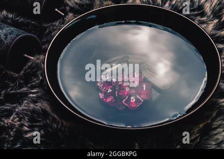Image of a dark ceramic bowl filled with water, pink dice, and crystals placed upon a brown fur. Stock Photo
