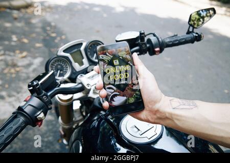 Hand of man sitting on motorcycle showing food delivery application on smartphone Stock Photo