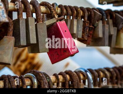 Red love lock with heart drawing, hanging on the bridge among other rusty locks. Stock Photo