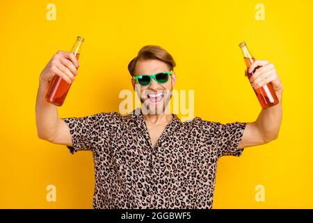 Photo of funky charming young guy wear leopard outfit dark eyewear drinking beer isolated yellow color background Stock Photo