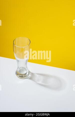 An empty beer glass placed on a white table in front of a yellow background Stock Photo