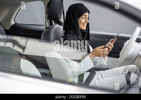 Muslim woman talks on phone while driving a car Stock Photo