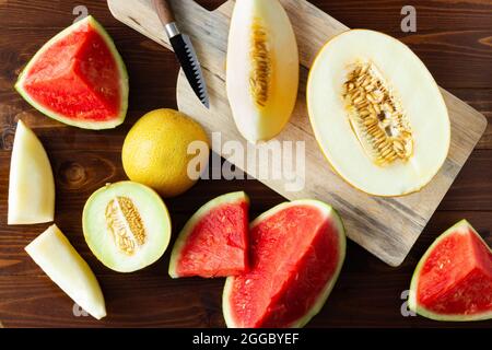 Top view of variety of cut melons and slices on wooden cutting board and rustic wood; summer fruits Stock Photo